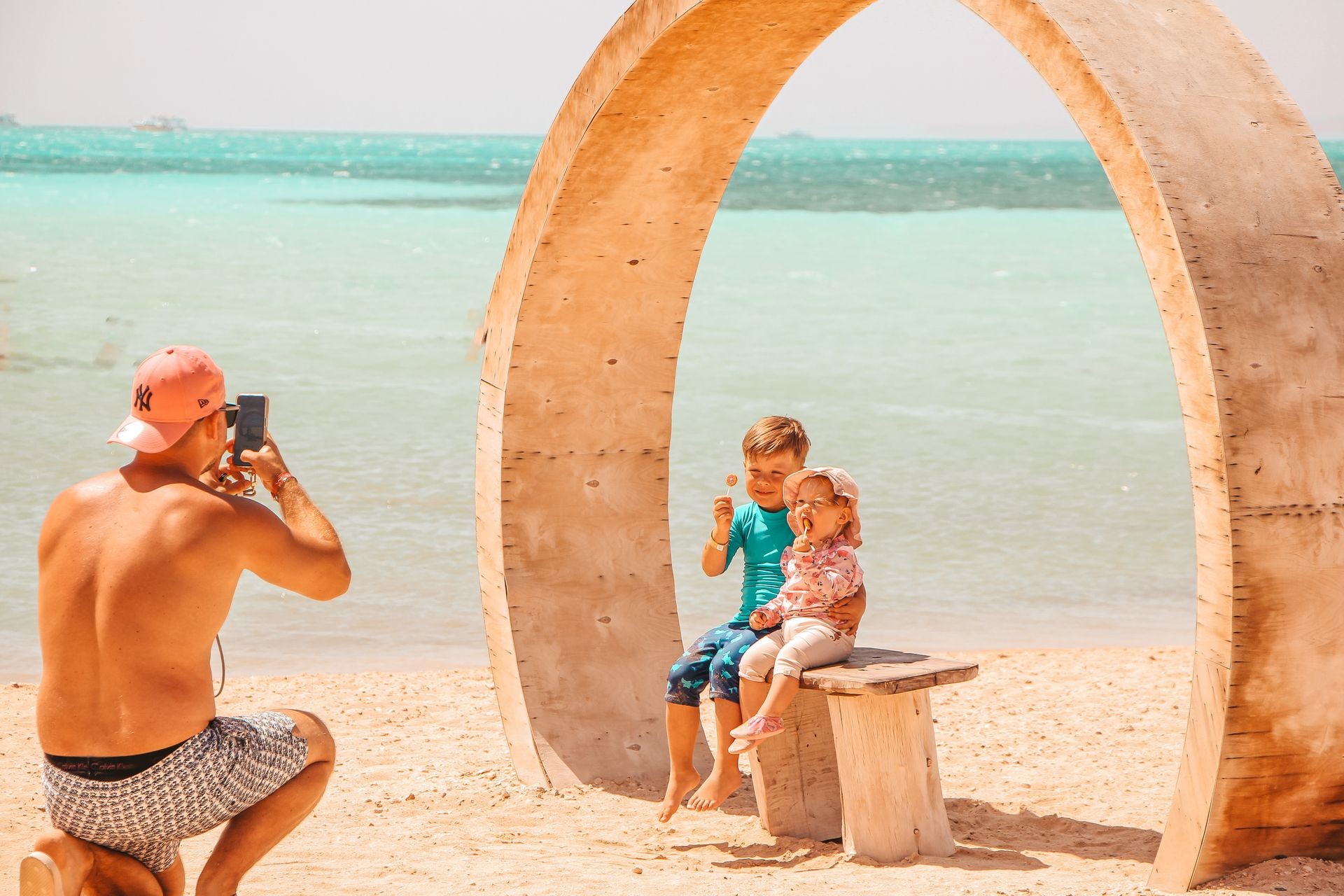 Familienfreundlicher Ausflug nach Orange Bay, Hurghada: Ein Mann fotografiert seine Kinder unter dem ikonischen Steinbogen auf der Insel Orange Bay, umgeben von weißem Sand und türkisblauem Meer. Der perfekte Instagram-Spot für Reisende, die einen entspannten Tag auf der schönsten Insel im Roten Meer verbringen möchten.