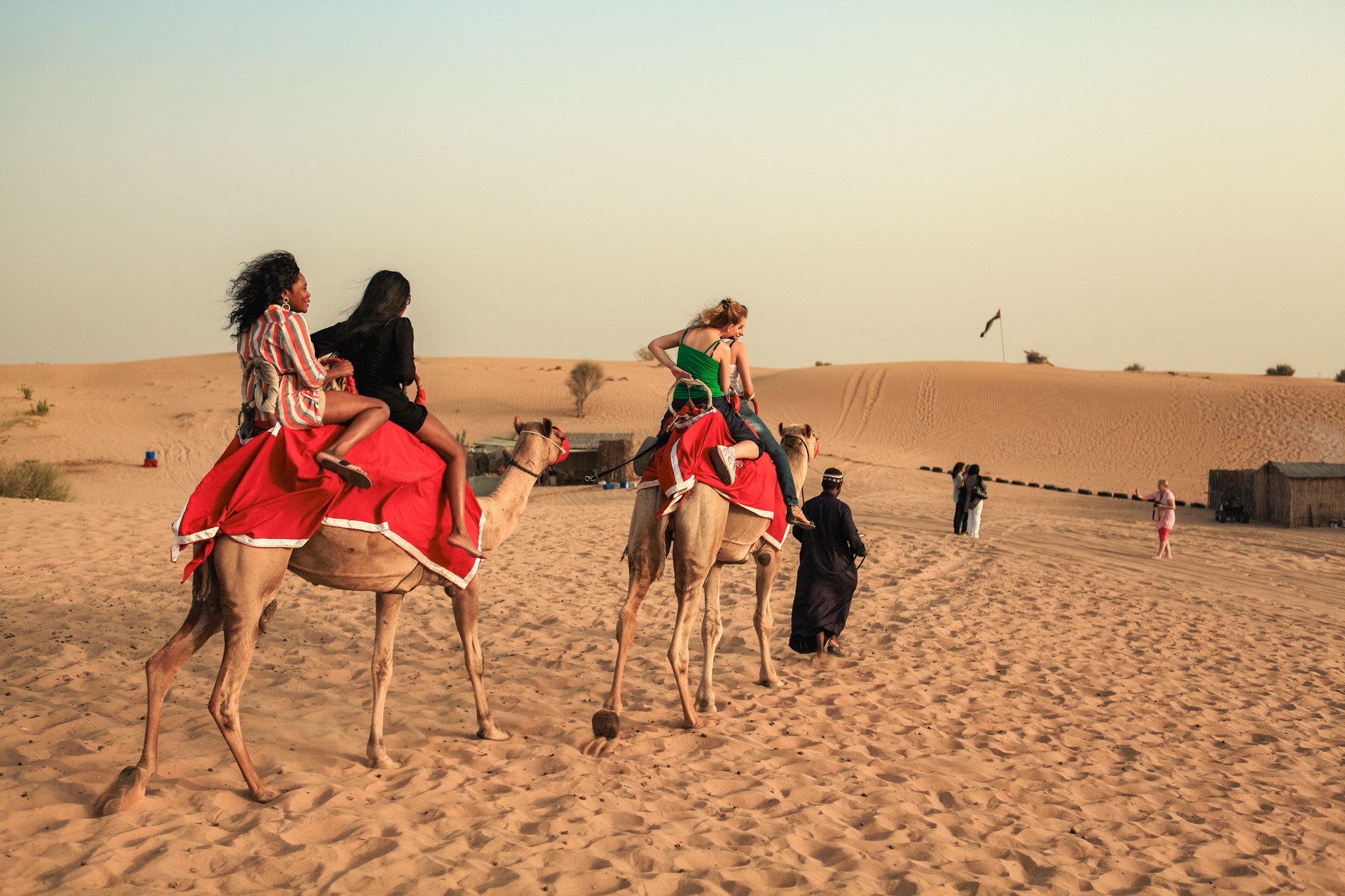 Riders enjoy a camel trek in the stunning desert landscape of Dubai UAE under the warm glow of the setting sun